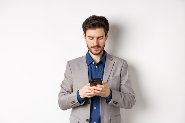 Empresario charlando por teléfono móvil, de pie en traje con cara seria, fondo blanco.