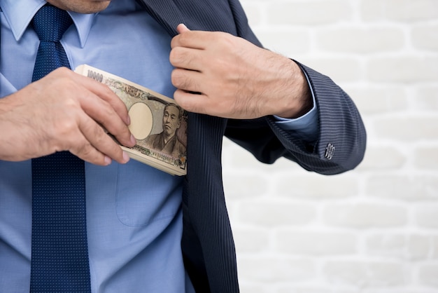 Empresário, colocando dinheiro, notas de ienes japoneses, no bolso do terno