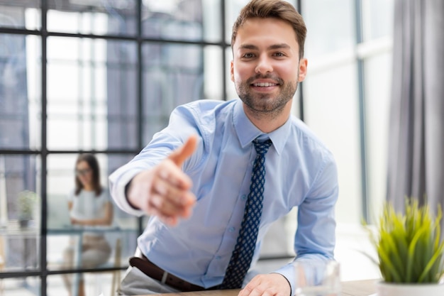 Empresário com a mão aberta pronta para selar um acordo no escritório com colegas no fundo