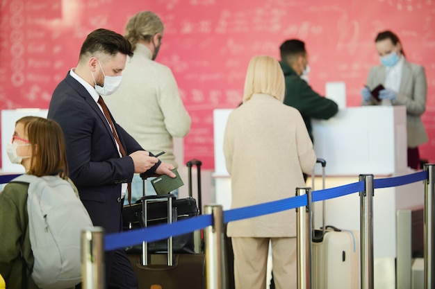 Empresário com bagagem indo para uma viagem de negócios, digitando uma mensagem no celular enquanto estava em uma fila no aeroporto