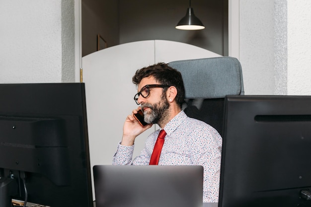 Empresário com barba e óculos falando ao telefone de seu escritório