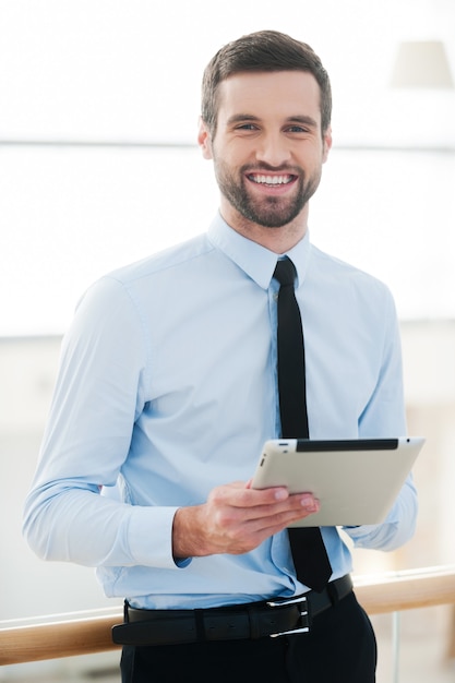 Empresário com bloco de notas. jovem empresário alegre segurando um tablet digital e sorrindo enquanto está dentro de casa