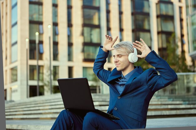 Empresário com fones de ouvido sem fio e laptop sentado perto do centro de negócios