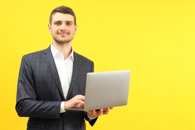 Empresário com laptop em fundo amarelo, espaço para texto.