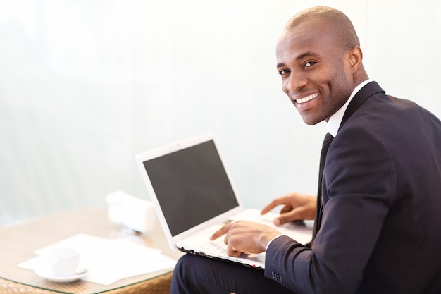 Empresário com laptop. jovem empresário africano digitando algo no laptop e olhando por cima do ombro