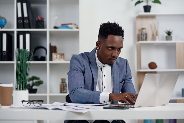 Empresário com laptop. Jovem empresário Africano está digitando algo no laptop em seu escritório.