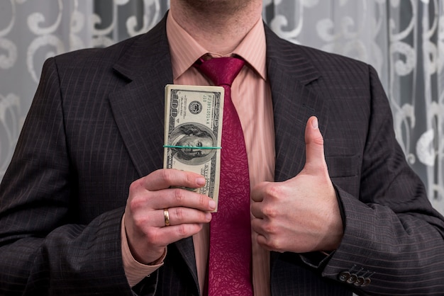 Foto empresário com notas de dólar em uma mão e polegar para cima