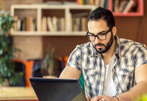 Empresário com óculos trabalhando com laptop na moderna sala de coworking elegante com pensamento inteligente de estantes