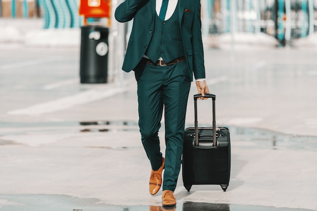 Empresário com roupa formal, puxando a bagagem e andando na rua. Conceito de viagem de negócios.