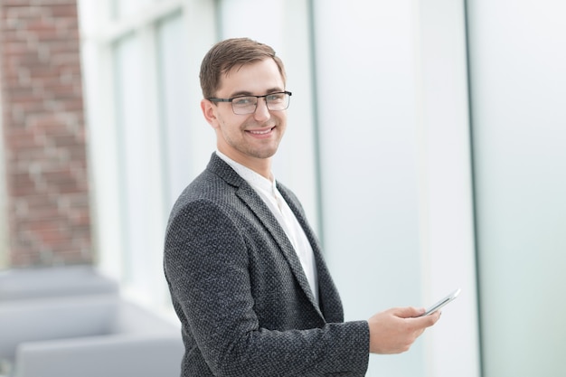 Empresário com smartphone em pé em um escritório luminoso.