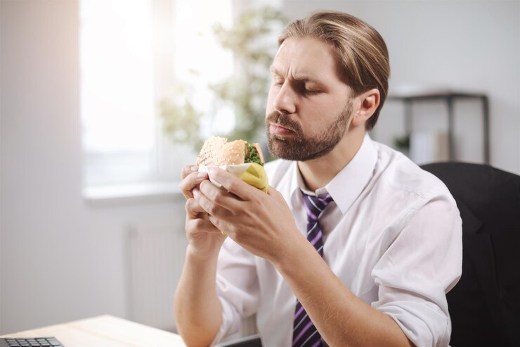 Empresario comiendo hamburguesa en oficina brillante