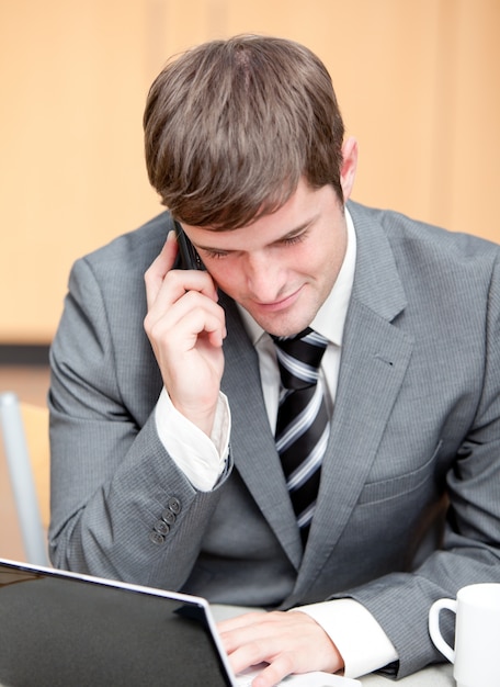 Empresário concentrado usando seu laptop enquanto fala no telefone