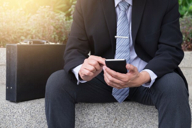Empresário confiante atraente, sentado em um terno preto e usando telefone inteligente