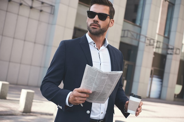 Empresário confiante e feliz jovem empresário lendo jornal do lado de fora do prédio de escritórios