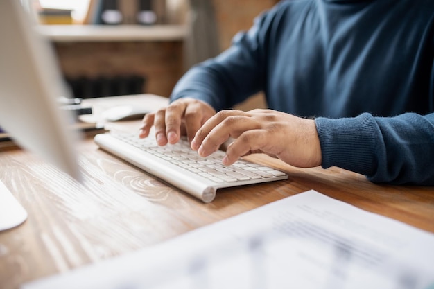 Empresário contemporâneo ou professor pressionando botões do teclado enquanto está sentado à mesa na frente do computador e trabalhando