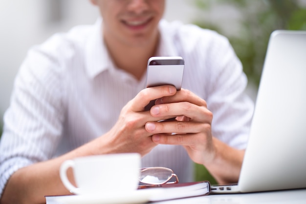 Empresário de camisa branca usando telefone móvel inteligente, navegando na Internet em um computador laptop