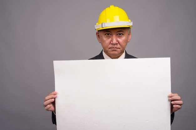 Empresário de construção asiático maduro contra parede cinza