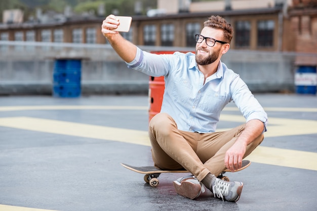 Empresário de hipster sentado com um telefone inteligente no playground do edifício industrial na cobertura. Conceito de negócio de estilo de vida