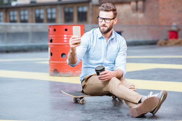 Empresário de hipster sentado com um telefone inteligente no playground do edifício industrial na cobertura. Conceito de negócio de estilo de vida