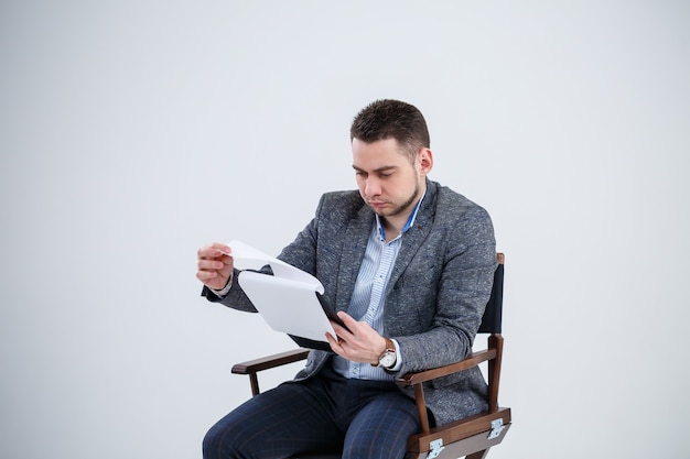 Empresário de homem de negócios de terno sentado em uma cadeira de madeira e joga documentos. Em um fundo branco com pensamentos sobre um novo projeto