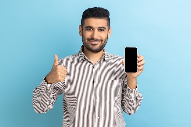 Empresário de pé segurando o telefone com display vazio mostrando polegares para cima com sorriso