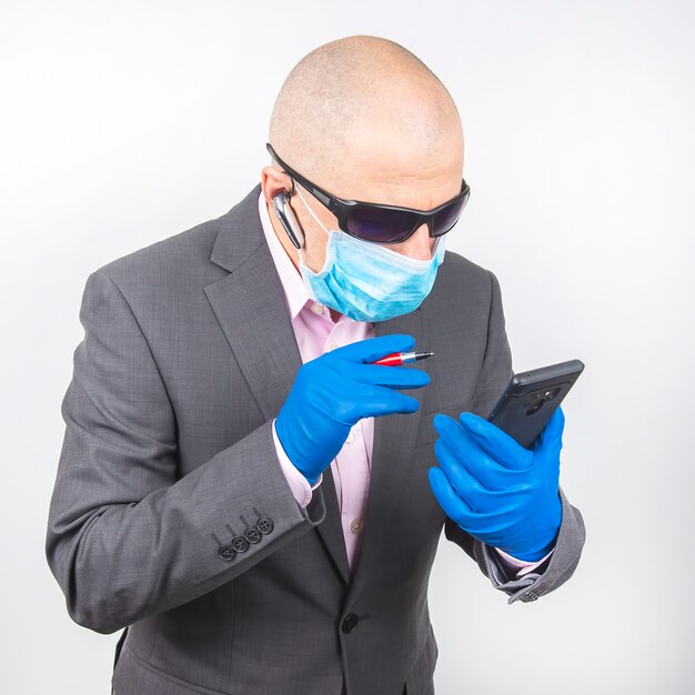 Empresário de sucesso com uma máscara protetora e luvas trabalha em um smartphone durante a quarentena do coronavírus. Trabalho freelancer online.
