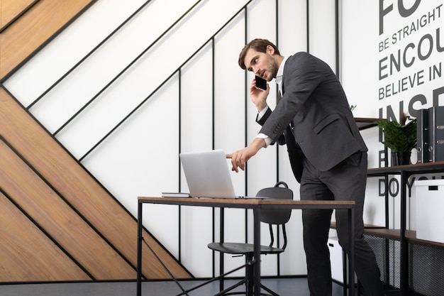 Empresário de sucesso falando ao telefone na área de trabalho com um laptop no escritório