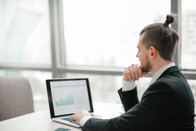 Empresário de sucesso trabalhando com gráficos financeiros no laptop.