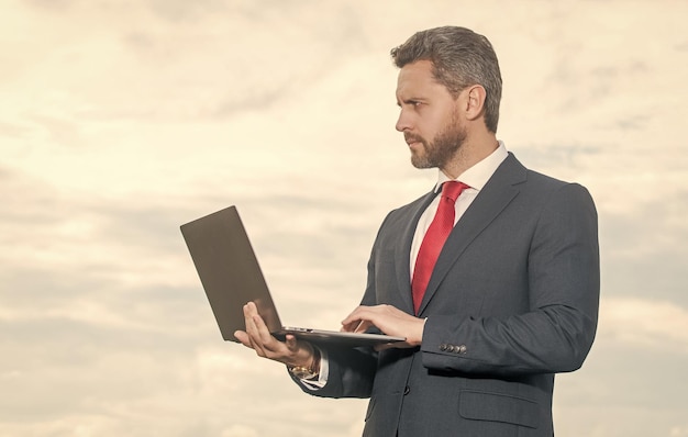 Empresário de terno usando laptop no fundo do céu