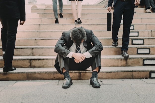 Empresario deprimido y cansado sentado en la escalera en la ciudad