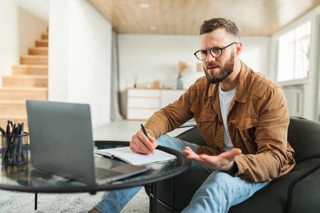 Empresario descontento usando una laptop tomando notas trabajando en línea en casa