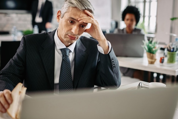 Foto empresario disgustado leyendo un correo electrónico en la computadora mientras come un sándwich en el trabajo