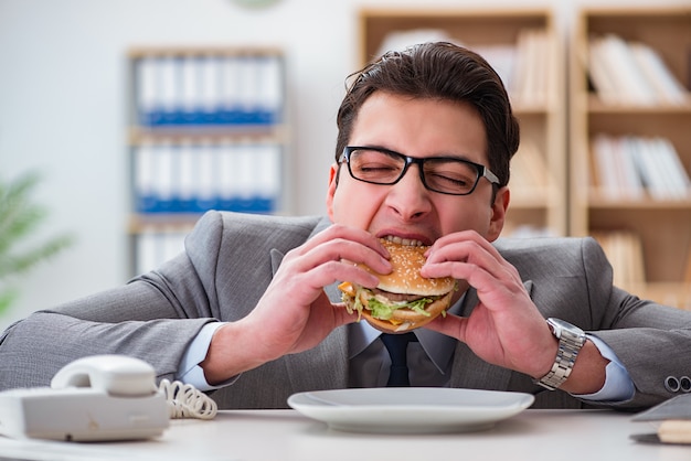 Empresario divertido hambriento comiendo sandwich de comida chatarra