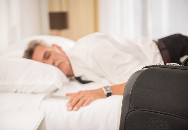 Empresario durmiendo en la cama después de un duro día de trabajo en la habitación del hotel Vista lateral