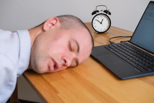 Empresario durmiendo en el escritorio al lado de la computadora portátil y el despertador