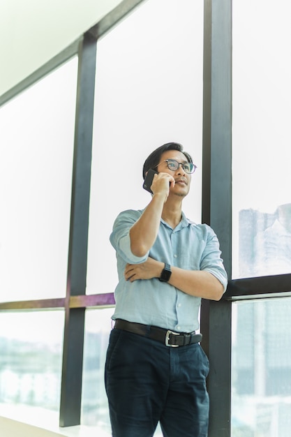 Empresário em pé ao lado de uma grande janela dentro de um prédio moderno falando no celular