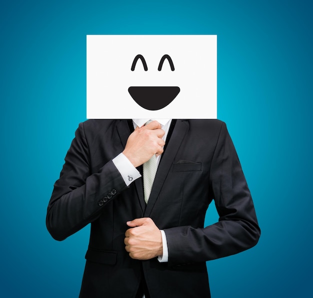 Empresário em pé, rosto de sorriso feliz de papel branco, segurando a frente da cabeça