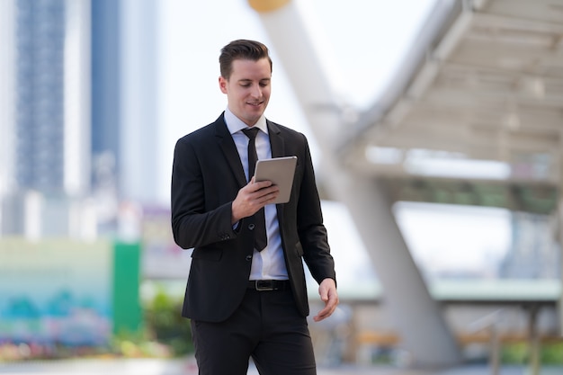 Empresário em pé usando um tablet digital em frente a edifícios de escritórios modernos