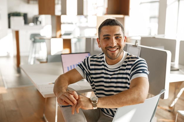 Foto empresário em roupas casuais trabalhando laptop enquanto está sentado em um escritório moderno no fundo dos colegas