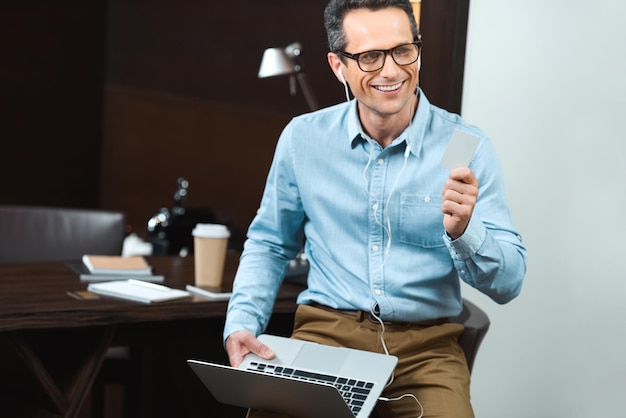 Empresário em roupas de negócios casuais segurando seu cartão de crédito e laptop