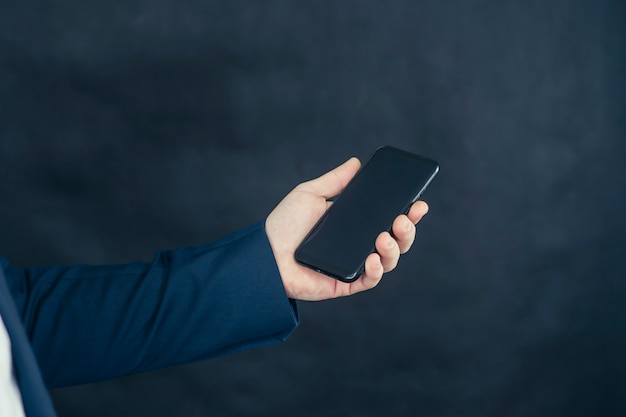 Empresário em uma camisa e um casaco azul com smartphone na mão.