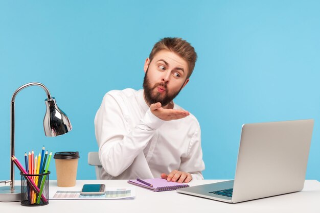 Empresario emocional trabajando en equipo portátil sobre fondo azul.