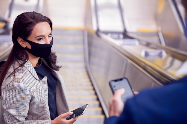 Empresario y empresaria montando escaleras mecánicas en la estación de tren usando máscara facial PPE en pandemia