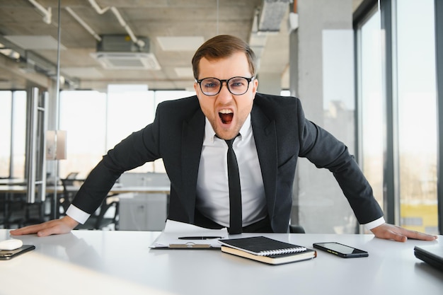 Empresario enojado sentado en su escritorio y gritando a sus empleados