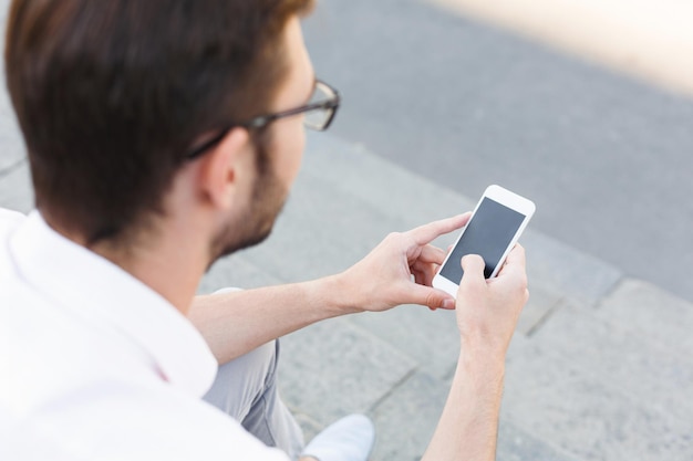 Empresario enviando mensajes de texto por teléfono móvil mientras está sentado en las escaleras de piedra, copie el espacio. Hombre en ropa formal con dispositivo digital, vista por encima del hombro. Concepto de negocio, tecnología y comunicación.