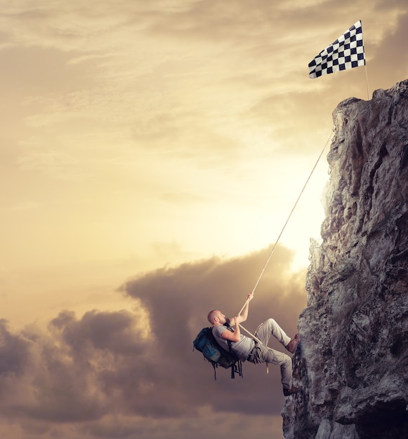 Empresário escala uma montanha com uma corda para pegar a bandeira. objetivo de negócios de realização e conceito de carreira difícil