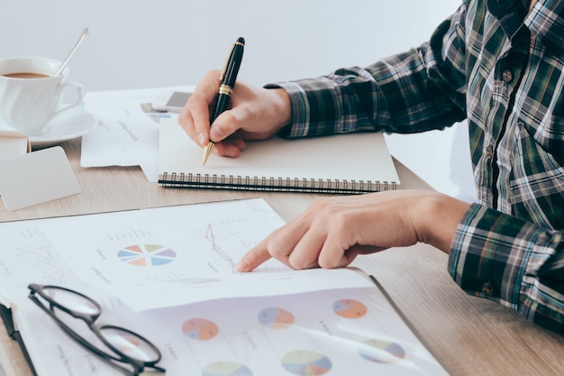 empresário escrevendo algo no caderno de papel e documento de relatório de finanças comerciais borrado na tabela, conceito de contabilidade
