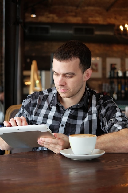 empresário está segurando um tablet digital e sentado em um café.