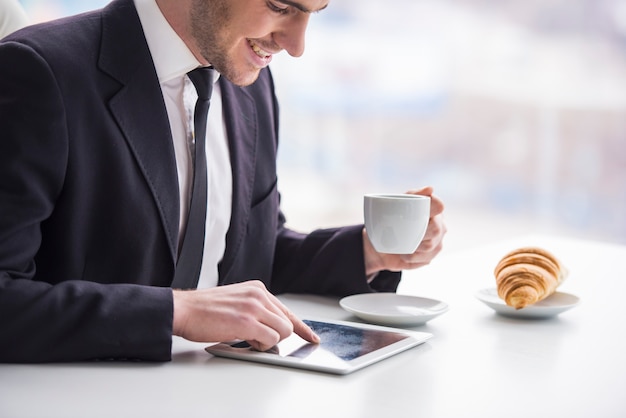 Empresário está trabalhando com tablet e bebendo café.