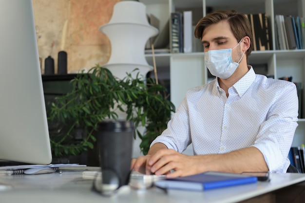 Empresário está trabalhando na máscara médica preventiva no escritório.